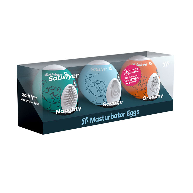 The Satisfyer Masturbator Eggs - Mixed 3 Pack #2 includes three stroker sleeves labeled "Naughty," "Savage," and "Crunchy." Each compact-sized egg features a unique design and is recommended for use with water-based lubricant. The transparent packaging displays all three cyber-skin masturbation devices.