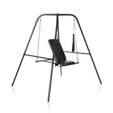 The Master Series Throne is an adjustable black swing set with a padded seat and straps hanging from a sturdy suspension frame. The minimalist design features chains connecting the seat to the top frame, supported by four legs in an A-frame structure.