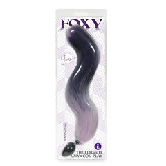 The image showcases the "Foxy Fox Tail Silicone Butt Plug," featuring a faux-fox tail with long, gradient colors transitioning from dark to light purple. The text underscores that it is a premium silicone plug, marketed as "The Elegant Way to Cos-Play.