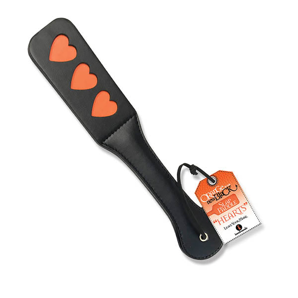 The 9's Orange Is The New Black Bondage Slap Paddle Hearts is a black leather paddle featuring three reverse cut red hearts and a tag attached to the handle. The tag reads: "Bare Heart" and includes additional text and branding details. Crafted from stitched PU leather, this paddle is perfect for sub role play.