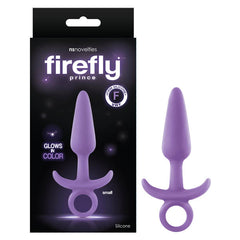 The image shows a Firefly Prince Butt Plug in purple, featuring a ring handle and flared base. It is presented next to its black packaging with purple text, highlighting "glows in color," "body-safe silicone," and "suitable for all lubricants." The product descriptions also mention assorted colors and sizes.