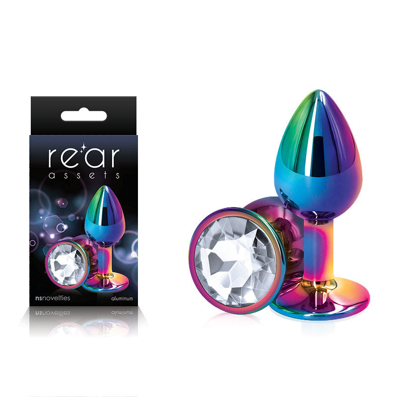 The image showcases the Rear Assets Multi Coloured Small Butt Plug, a metallic chrome-plated butt plug adorned with a clear, faceted jewel at the base. The item is displayed twice: once inside its black packaging and once outside. The packaging features branding that reads "Rear Assets" and promotes their body-safe anal toys.