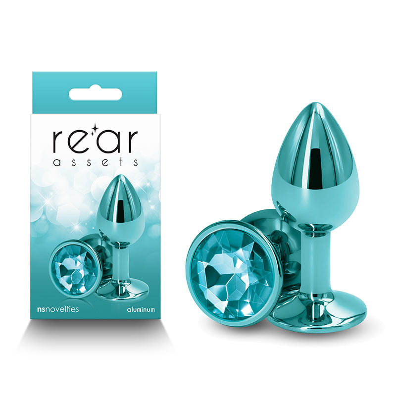 A packaged set of lightweight aluminum, teal anal toys with a gemstone finish on the base. The packaging displays the brand name "Rear Assets - Small - Teal" and showcases the body-safe product. The plugs are shown both inside the packaging and separately on the right side.