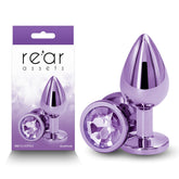 Image features a package and product from the brand "nsnovelties." The Rear Assets - Medium Butt Plug - Purple is a shiny, lightweight aluminum plug with a jewel-like end. Showcasing high-end body-safe materials, the plug is displayed both inside its purple and white packaging and outside of it on the right.
