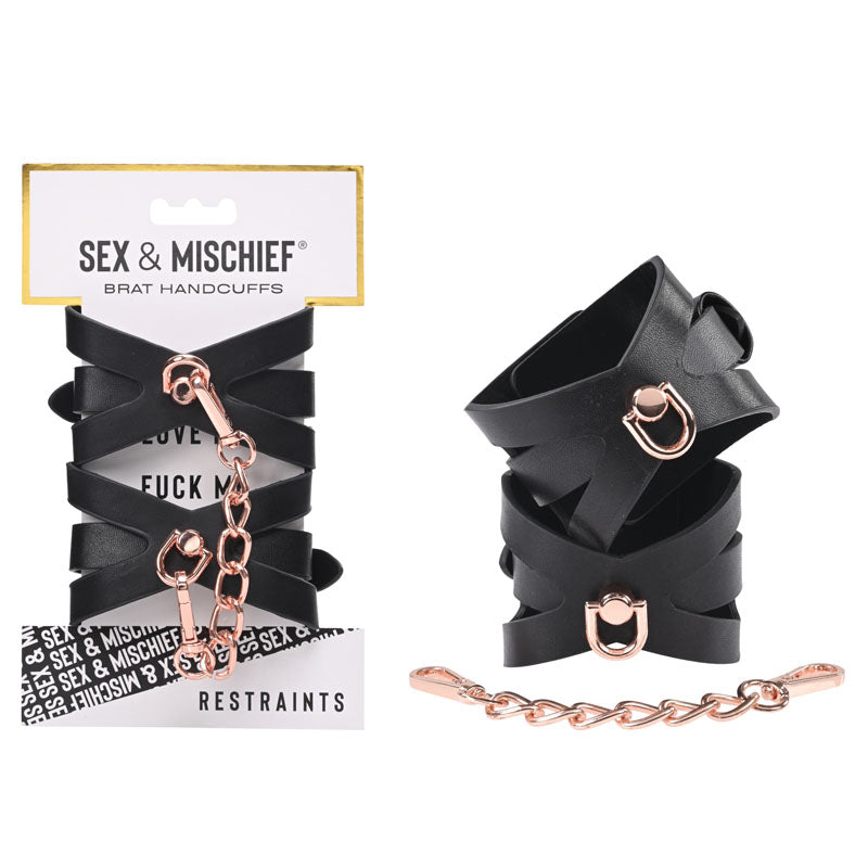 The packaging of the "Sex & Mischief Brat Handcuffs" features two black faux leather handcuffs adorned with rose gold-colored chains and hooks. The top of the package displays the product name, while "Restraints" is indicated at the bottom. One cuff is shown open and the other is closed, connected by an elegant rose gold chain.