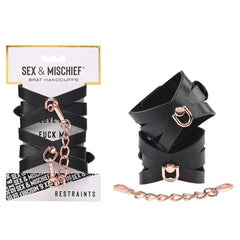 The packaging of the "Sex & Mischief Brat Handcuffs" features two black faux leather handcuffs adorned with rose gold-colored chains and hooks. The top of the package displays the product name, while "Restraints" is indicated at the bottom. One cuff is shown open and the other is closed, connected by an elegant rose gold chain.