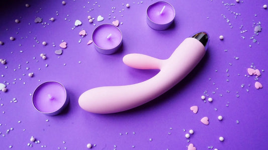 Purple g-spot vibrator in front of a purple back ground and next to 3 purple coloured tea light candles