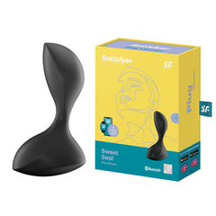 A black, curved anal plug vibrator with a powerful motor is displayed next to its packaging box. The primarily yellow box with blue accents features the brand name 'Satisfyer' and the product name 'Satisfyer Sweet Seal - Black Vibrating Butt Plug.' The waterproof packaging also highlights app compatibility and other product details.