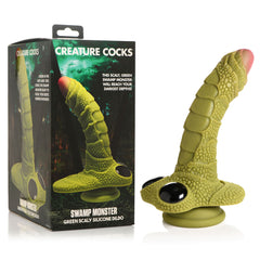 A product image showcasing the Creature Cocks Swamp Monster dildo, made of premium silicone and designed to resemble a green scaly swamp creature. It stands upright on a suction base next to the packaging box, which features the product name "Creature Cocks Swamp Monster" and descriptive text from Creature Cocks.