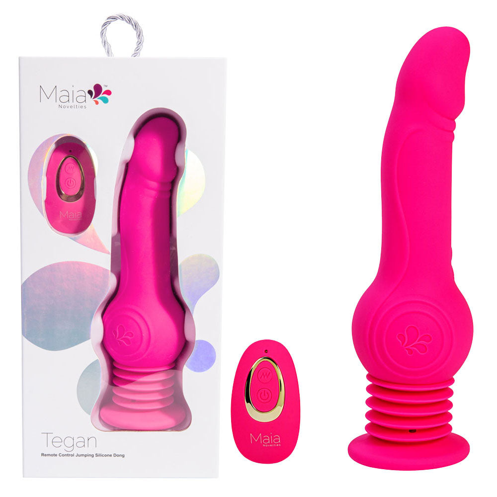 The Maia TEGAN, a pink silicone dildo crafted from medical-grade silicone, is showcased with its white packaging box and a rechargeable remote control. The dildo features a ribbed base and a slightly curved top. The packaging has a transparent window that reveals the product inside and is adorned with colorful floral designs.