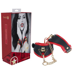A box of the OUCH! Milan Collection - Handcuffs featuring a black and white image of a woman with makeup on the front. Beside the box, a pair of black and red handcuffs made from bonded leather with gold-colored hardware and a connecting chain is displayed.