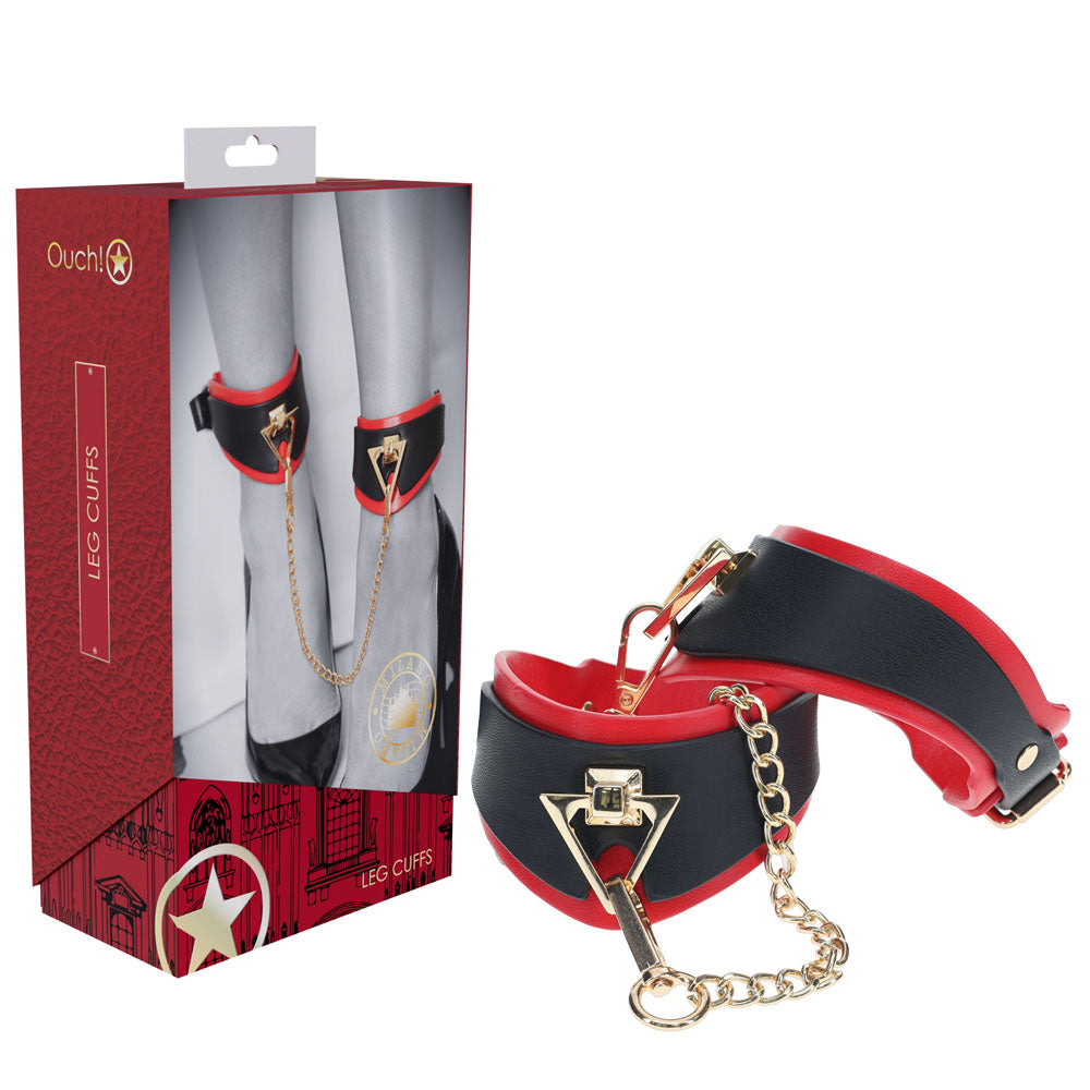 A pair of black and red bonded leather OUCH! Milan Collection Leg Cuffs, connected by a golden chain, are displayed next to their packaging box. The box features an image of the cuffs in use on a pair of ankles and includes branding and product details, exuding an air of high fashion.