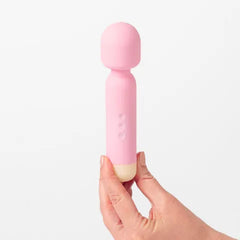 Pink handheld massager held in a hand against a white background