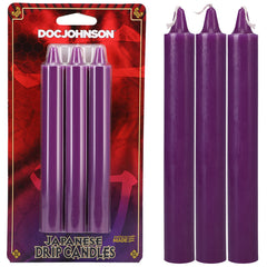 A packaged set of three Japanese Drip Candles - Purple from Doc Johnson. The red packaging with yellow accents prominently displays the brand name. Perfect for hot wax play, next to the package are three identical individual purple candles ready for use.