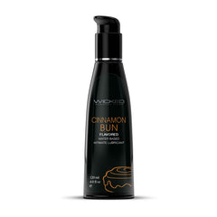 A black bottle with a pump dispenser labeled "Wicked Aqua Cinnamon Bun" in green text. Below it, "Cinnamon Bun Flavored Water Based Lubricant" is written in orange text. Perfect for oral pleasures, the 120 ml (4 fl oz) bottle features a small cinnamon bun graphic at the bottom.