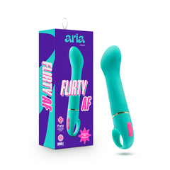 A teal-colored Aria Flirty AF personal massager, featuring a loop handle and pink buttons, is displayed alongside its vibrant purple-and-pink packaging. The box, branded "Aria by Blush," showcases the waterproof vibrator, emphasizing its "Purio Silicone" material and "10 Intense Vibrations" features.