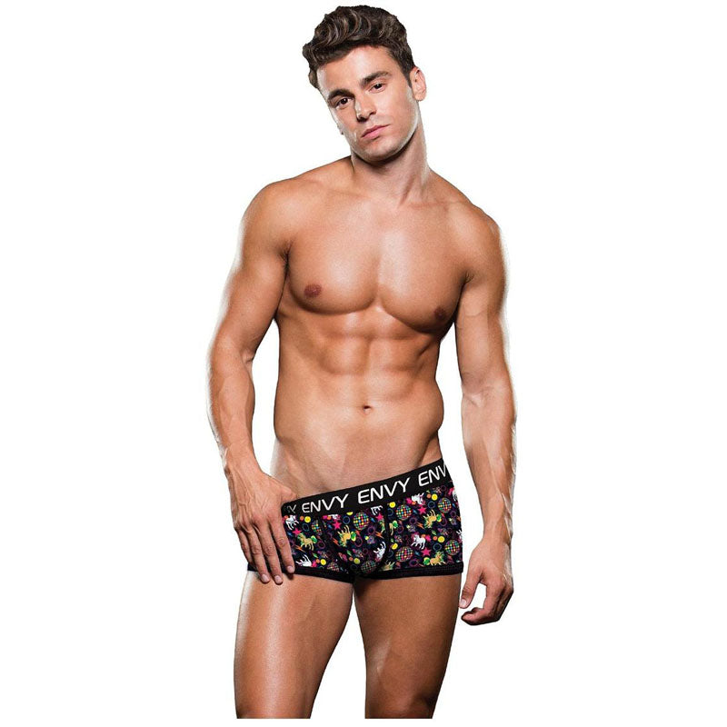 A muscular man stands in the ENVY Disco Unicorn Trunk - M/L, black boxer briefs adorned with a vibrant floral pattern evocative of a field of unicorns. The waistband features "ENVY Menswear" in white letters. He gazes toward the camera with a neutral expression against a white backdrop.