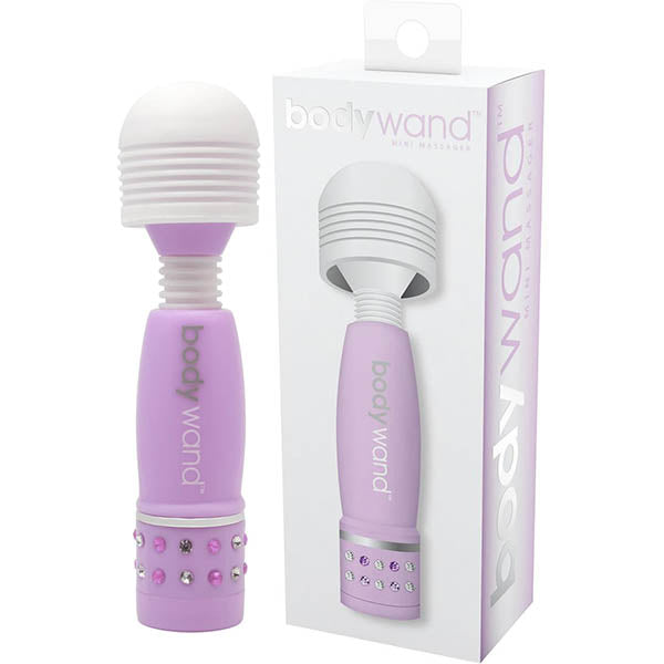 The image shows the Bodywand Mini - Lavender Mini Massager Vibrator, featuring a purple body, soft-touch white head, and gem accents at the base, positioned next to its packaging. The packaging displays an image of the massager with "body wand" written in light purple text. This device offers multi-directional usage for strong stimulation.