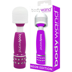 A Bodywand Mini Massager Neon Edition Purple, featuring a white, soft-touch head and rhinestones near the base, is displayed next to its matching box. The box reads "bodywand mini massager, neon edition" and showcases an image of the massager. This splashproof device provides strong stimulation while maintaining a stylish appearance.