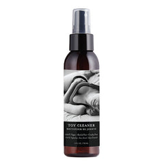A black spray bottle labeled "Hemp Seed Toy Cleaner" features a black-and-white image of a person lying down on the label. The 4 fl oz (118 mL) bottle is 100% vegan, alcohol-free, cruelty-free, and safe for all toy materials, offering advanced cleaning action for safe and effective results.