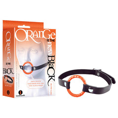 A black silicone strap with an orange-ringed blow-gag and adjustable buckle is displayed next to its packaging. The packaging reads "Orange is the New Black - Blow Gag" and "Black/Orange Open Mouth Gag with Sturdy Straps" and includes an image of the product in use, perfect for your bondage fetish collection.