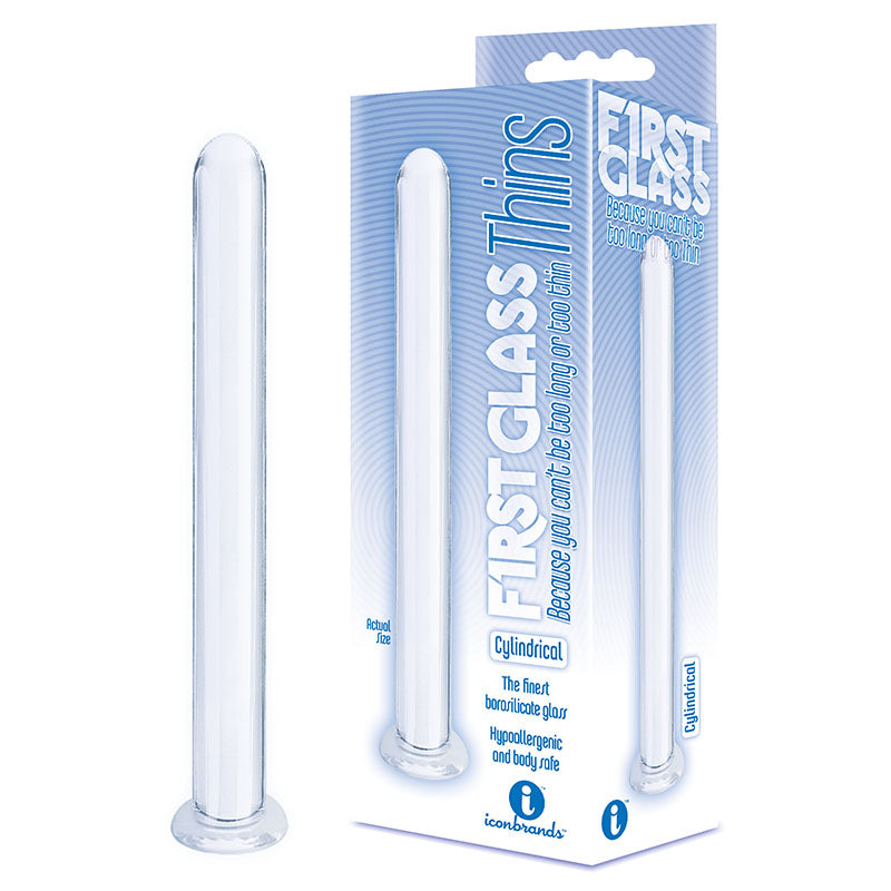 A transparent cylindrical glass massager, identified as "The 9's First Glass Thins, Cylindrical - Clear Glass 17.8 cm Dildo," is shown next to its blue and white packaging. The packaging reads "FIRST GLASS" and "Thins Cylindrical, Hypoallergenic and body safe," featuring a clear window that displays the borosilicate glass product inside, ideal for temperature play.