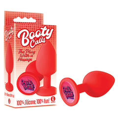 A red silicone butt plug labeled "The 9's Booty Calls Butt Plug - Fuck Yeah" is displayed alongside its packaging. The base of the plug features the inscription "Fuck Yeah" on a glittery pink background. The packaging also highlights "100% Silicone, 100% Fun!