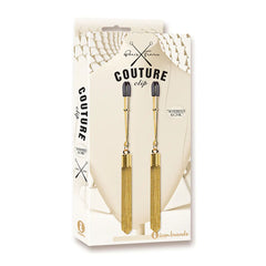 A product image of the "Couture Clip - Shimmer & Chic" by Icon Brands. The package features two elegant nipple clips with golden mesh, designed for intimate use. The backdrop shows a geometric white pattern, and the words "Shimmer Chic" are printed on the right side of the package.