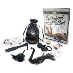 The "Behind Closed Doors - Weekend In Bed" kit for lovers includes an eye mask, a feather tickler, a flogger, a paddle, a satin storage pouch, a tealight candle, dice, and various cards and instructions spread out on a white background. Perfect for transforming any romantic location into an unforgettable escape.