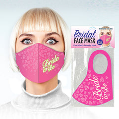 A person with light blonde hair is wearing the "Bridal Face Mask - Bride To Be," a cute and risqué pink mask adorned with the phrase "Bride to Be" in yellow. Next to them is its packaging, highlighting the naughty pattern face covers with diamond designs and promoting it as a "Fun & Sexy Novelty Mask.