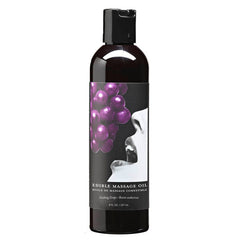 A black bottle with a black flip-top lid contains vegan edible massage oil. The label features an image of a woman's face with her mouth open, approaching a bunch of purple grapes. Text on the label reads "Edible Massage Oil - Gushing Grape Flavoured." The bottle is 237 ml / 8 fl oz.