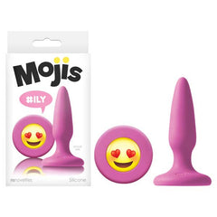 The image showcases the Mojis Butt Plug - #ILY, a pink silicone butt plug featuring a heart-eyes emoji on the base. It is displayed next to its packaging, which is branded "Moji’s" and features the hashtag "#ILY" on a white background—perfect for exploring new dimensions in butt-play.