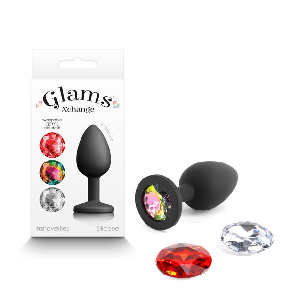 A black silicone butt plug from the "Glams Xchange Round - Small" collection is displayed alongside two interchangeable round gem pieces, one in red and the other in clear. Crafted from premium grade silicone, the packaging is visible and labeled "Glams Xchange," featuring images of this fashionable accessory with its vibrant interchangeable gems.
