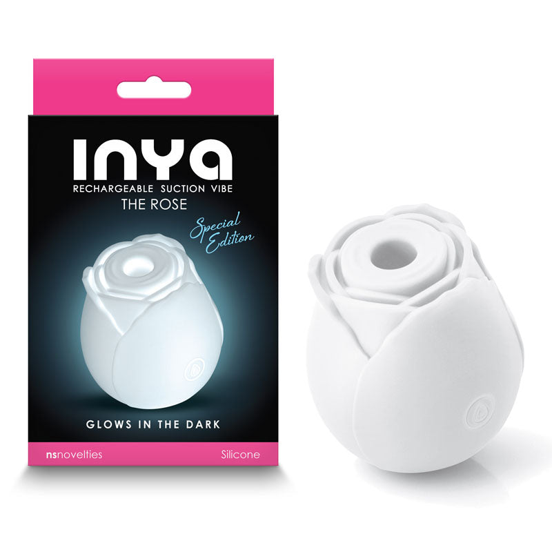 A product image of the INYA The Rose Clitoral Vibrator - Glow, Special Edition. The vibrator, crafted from body-safe silicone and shaped like a rose, features a white color that glows in the dark. It is displayed alongside its pink and black packaging which highlights the product name and details.