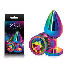 A product image showing a metallic, rainbow-colored Rear Assets Multi Coloured Medium Metal Butt Plug with a gem-like base, displayed next to its packaging. The packaging features the same product image and the text "rear assets." This chrome-plated anal toy ensures both elegance and safety in your intimate moments.