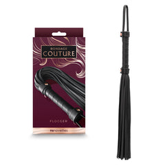 A black Bondage Couture Flogger by NS Novelties, displayed next to its packaging adorned with decorative swirls and branded as "Bondage Couture." The packaging labels it as a "Flogger," promoting it as the ultimate accessory for your collection.