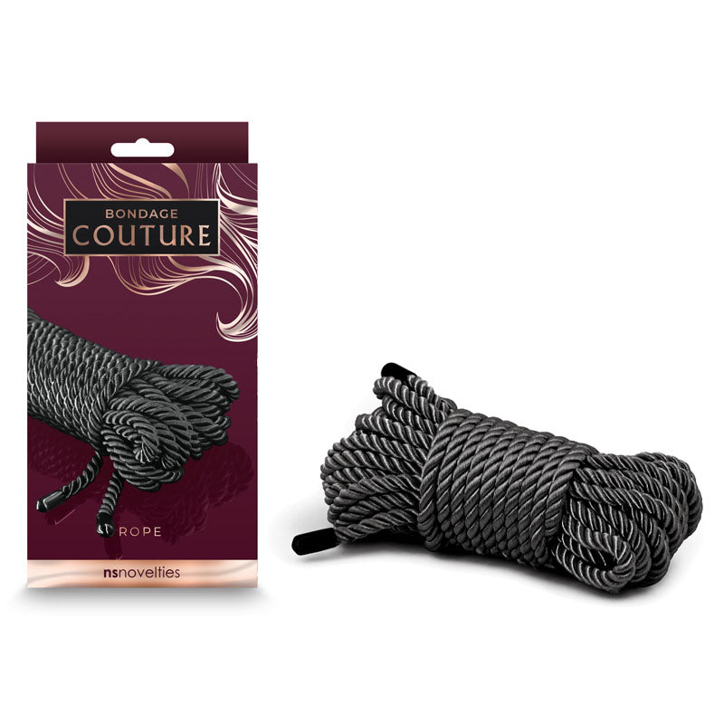 A package labeled "Bondage Couture Rope - Black" featuring an image of coiled black and white synthetic rope. Beside the package is a real bundle of the same type of rope, tied in a compact coil. The dark burgundy packaging showcases NS Novelties' signature decorative elements.