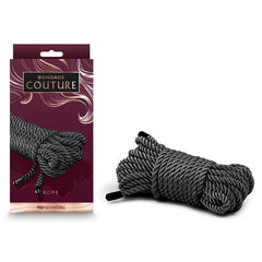 A package labeled "Bondage Couture Rope - Black" featuring an image of coiled black and white synthetic rope. Beside the package is a real bundle of the same type of rope, tied in a compact coil. The dark burgundy packaging showcases NS Novelties' signature decorative elements.