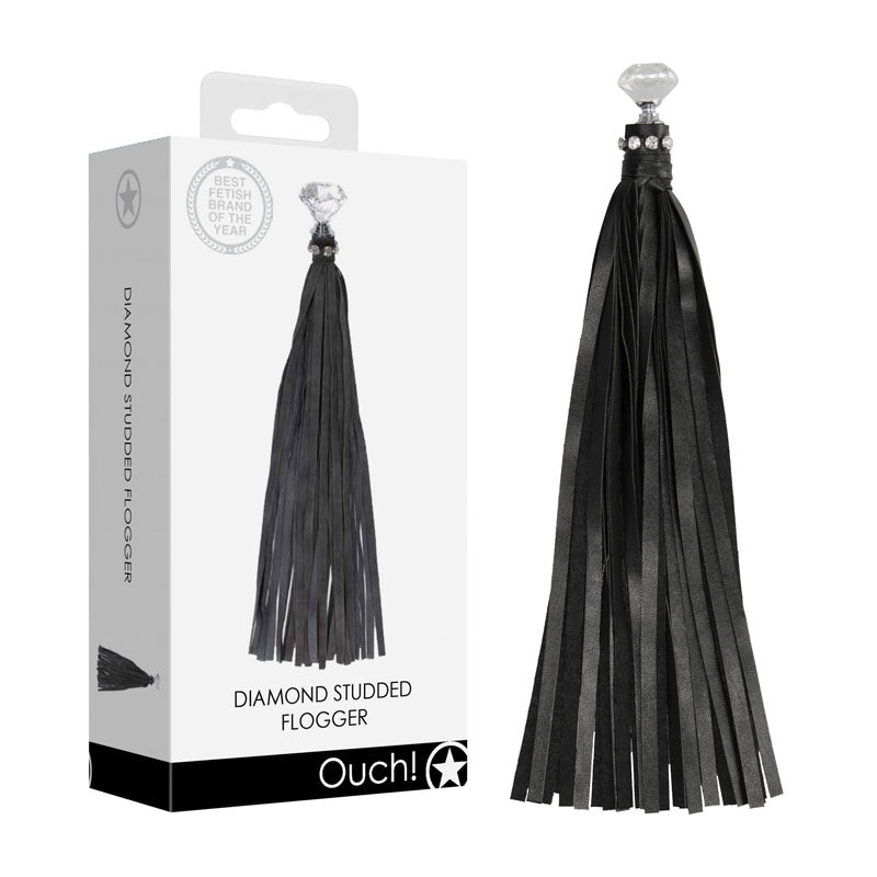 A black, diamond-studded whip with long leather straps is displayed next to its packaging. The package features an image of the whip and includes text reading "OUCH! Diamond Studded Whip" at the bottom, accompanied by a star symbol.