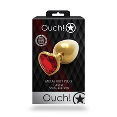 A product image of the "OUCH! Heart Gem Gold Butt Plug - Large." The plug is gold with a heart-shaped, jewel-encrusted base featuring a ruby-red gemstone. Perfect for temperature play, the black packaging showcases the brand name, product description, and an award badge for "Best Fetish Brand of the Year.