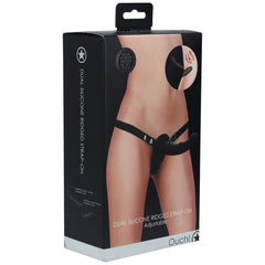 A product box labeled "OUCH! Dual Silicone Ridged Strap-On Dildo - Black" features a photo of a person wearing the strap-on device on the front. The text highlights its adjustability, construction from medical-grade silicone, and manufacture by the brand "Ouch!" The predominantly black and white packaging includes additional product details.