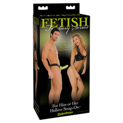 Packaging for the "Fetish Fantasy 6" Hollow Strap-on Dildo - Glow in the Dark." The box features an image of a man and a woman, both partially undressed and smiling. The product includes an adjustable elastic harness with straps and a hollow dildo. The packaging is by the brand Pipedream.