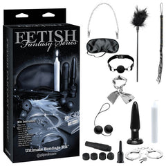 Image of the "Fetish Fantasy Series Limited Edition Ultimate Bondage Kit" by Pipedream. This all-in-one kit transforms any space into an erotic playground with a mask, ball gag, feather tickler, restraints, whip, candles, dildos and plugs, nipple clamps, and handcuffs—all displayed next to the box.