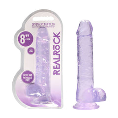 Packaging and product view of the RealRock 8'' Realistic Dildo With Balls. The dildo is translucent, purple in color, and features realistic balls along with a suction cup base. The packaging indicates it is 8 inches (19 cm) long, super flexible, and free of latex and phthalates.