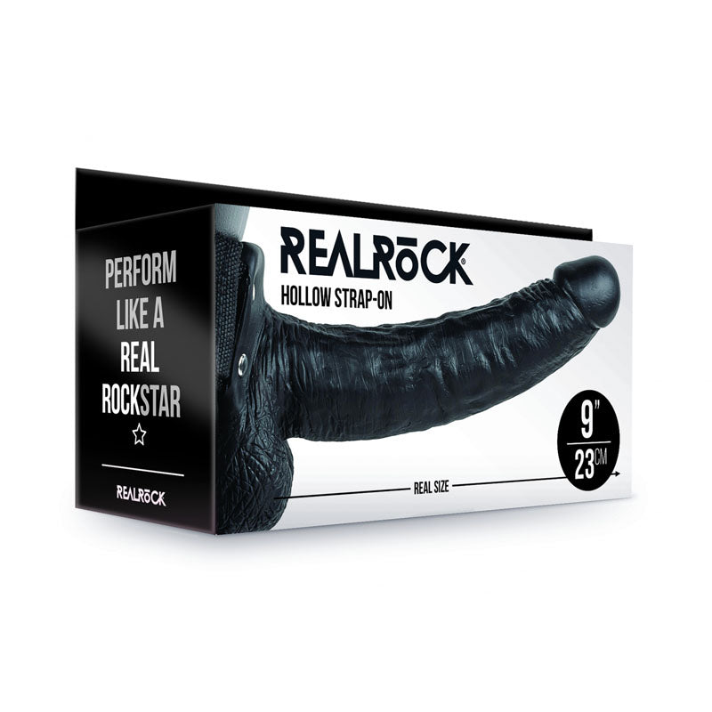 The image showcases box packaging for the "REALROCK Hollow Strapon with Balls - 23 cm Black." The design prominently displays the product's name and features an adjustable strap-on with a realistic black dildo, advertised as "23 cm" in size. The tagline reads, "Perform like a real rockstar.