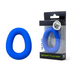A blue, oval-shaped silicone ring, identified as the "Sport Fucker Hero Ring Cock Ring - Blue," is placed beside its packaging. The transparent packaging displays the branding and text with a visible metallic seal on the top right corner. Made from liquid silicone, the product features an ergonomic design and is labeled "Sport Fucker.
