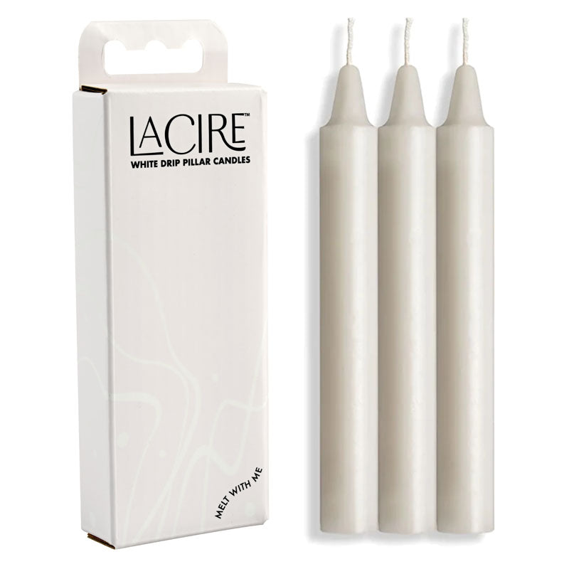 The image features a box labeled "LaCire Drip Pillar Candles - White" on the left and three upright white cylindrical candles on the right. Crafted from body-safe paraffin wax, these sensual drip candles are ideal for temperature play. The box is predominantly white with a minimalist design and text.