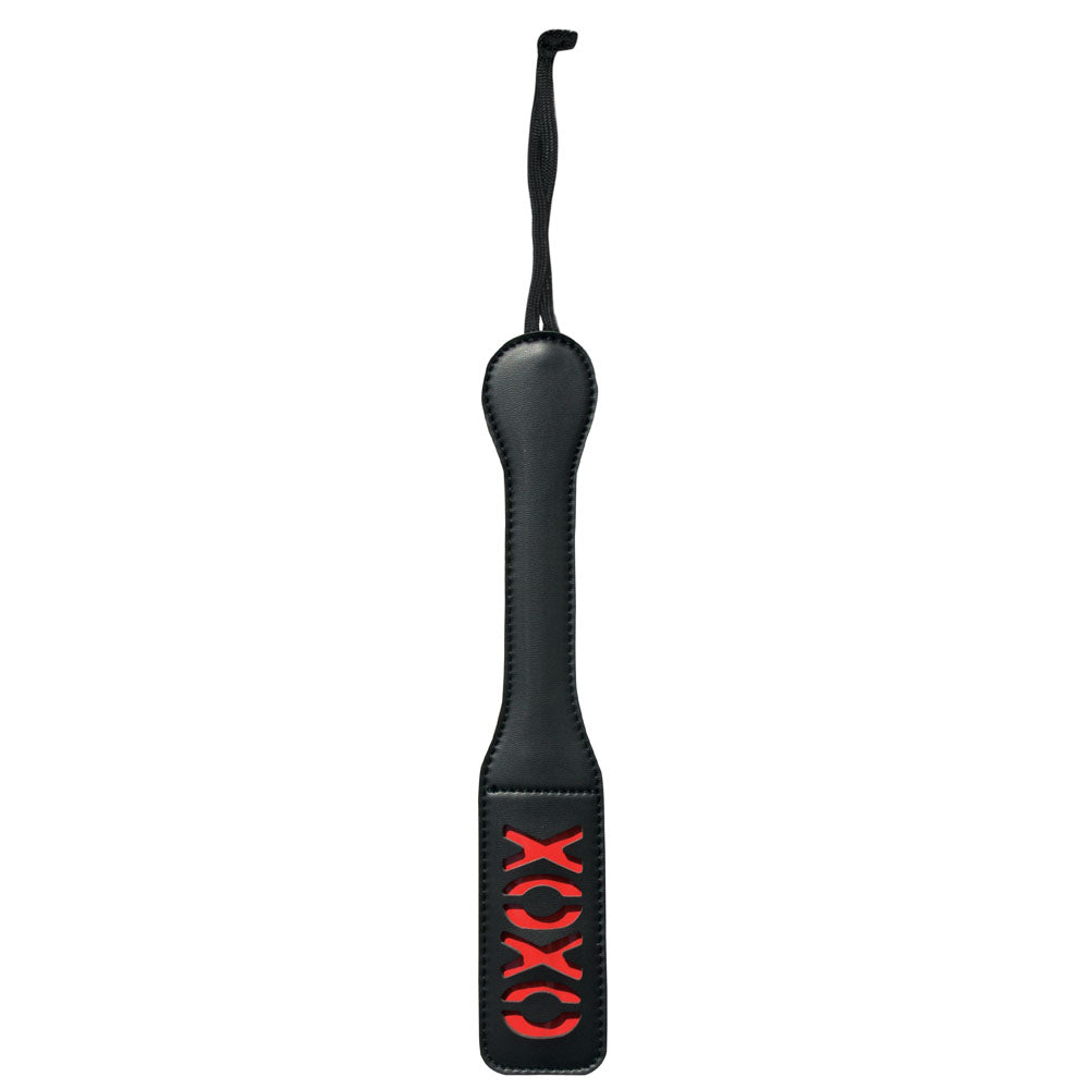 The Sex & Mischief XOXO Paddle - Black is a vinyl paddle featuring a sexy "XOXO" design cut out near the end. It has a wider end for impact and a narrow handle with a black wrist strap for grip.