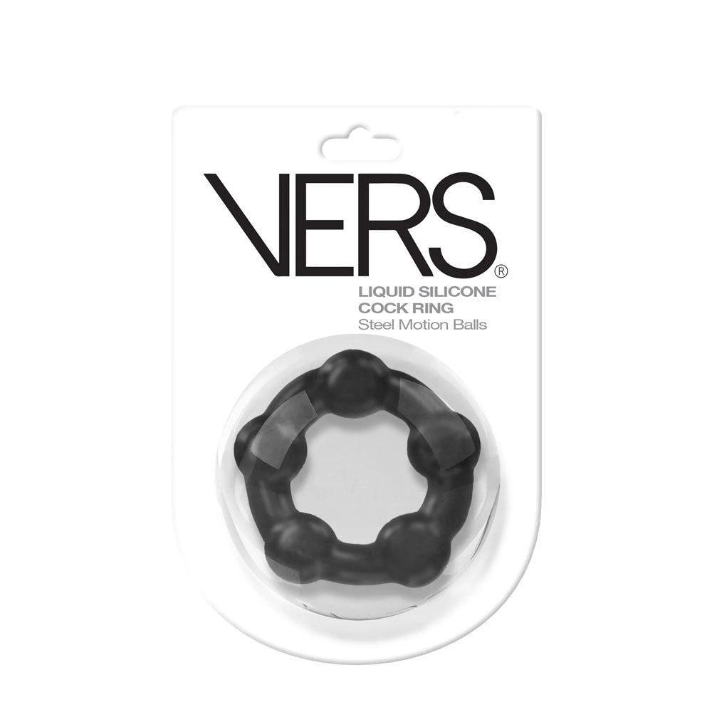 The image depicts the VERS Liquid Silicone Steel Motion Cock-Ring in its original packaging. The black ring includes several rounded protrusions designed to enhance sexual performance. The packaging is white with black text and features a clear plastic front that showcases the product.
